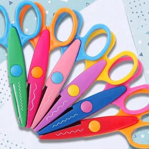 May include: A set of six decorative craft scissors arranged in a fan shape. Each pair features plastic handles in bright colors including blue, orange, pink, yellow, and red, with matching circular pivot points and zigzag or wavy cutting blades.