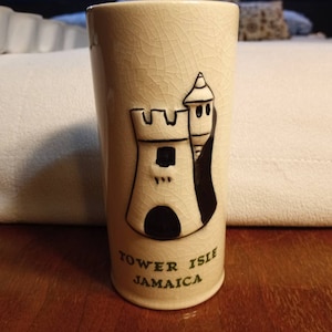 May include: A beige ceramic mug with a black and white illustration of a tower with the text "Tower Isle Jamaica" on the bottom.