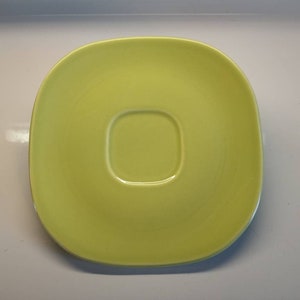 May include: A bright yellow ceramic saucer with a slightly raised center for a cup.
