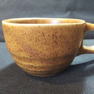 May include: A brown ceramic coffee mug with a speckled glaze and a rounded shape. The mug has a handle on the right side.