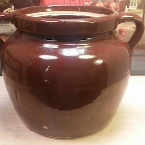 May include: A brown glazed ceramic crock with two handles. The crock is round and has a wide mouth.