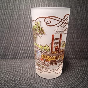 May include: A frosted glass with a detailed illustration of a steamboat, trees, and buildings. The design includes brown swirls at the top and the text "Currier & Ives" at the bottom. The glass is cylindrical.