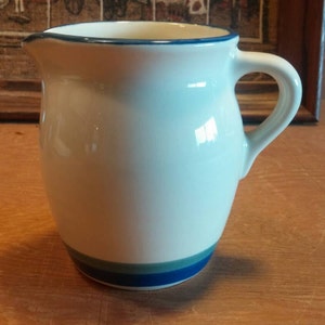 May include: A white ceramic pitcher with a blue rim and blue and green stripes around the bottom.