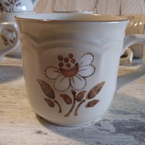 May include: A white ceramic mug with a brown floral design. The mug has a handle and a rounded shape.