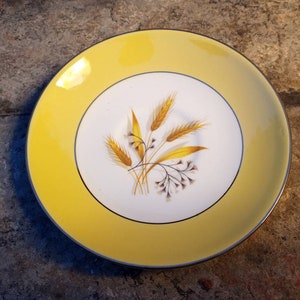 May include: A yellow saucer with a white center featuring a gold wheat design. The saucer has a gold rim.
