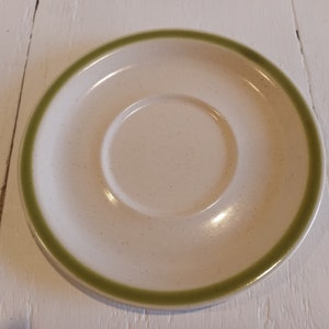 May include: A white saucer with a green rim. The saucer has a slight speckled texture.