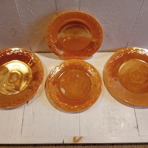 May include: Four orange glass plates with a leaf design. The plates are all the same size and have a glossy finish.