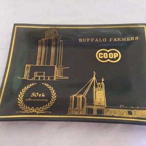 May include: Black glass ashtray with gold trim and a gold design of grain silos and the text "Buffalo Farmers Coop 50th Anniversary".