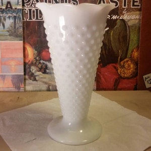 May include: A white milk glass vase with a textured, dotted surface. The vase has a flared top and a round base.