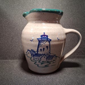 May include: A white ceramic mug with a black handle and the text "But First, Coffee" in a handwritten style. The mug is on a white surface. The mug is approximately 4 inches tall.