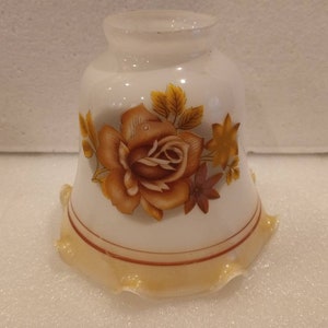 May include: A vintage-style, white glass lampshade with a floral design. The shade features a large, detailed rose in shades of brown and yellow, with matching leaves. The bottom edge has a scalloped design with a light yellow trim.