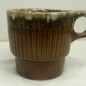 May include: A brown and white ceramic mug with a ribbed design and a handle. The mug has a speckled glaze.