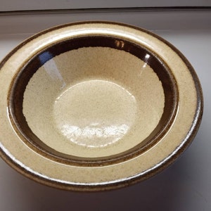 May include: A brown and beige ceramic bowl with a textured surface. The bowl has a wide rim and a deep well.