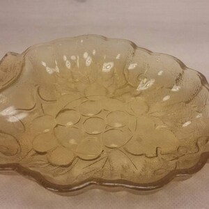 May include: A clear glass bowl with a grape design. The bowl is shaped like a bunch of grapes and has a scalloped edge.