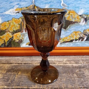 May include: A dark brown glass goblet with a fluted design. The goblet has a tall stem and a round base.
