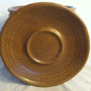 May include: Set of four brown ceramic saucers with a speckled glaze. The saucers have a slightly raised rim and a smooth, glossy finish.