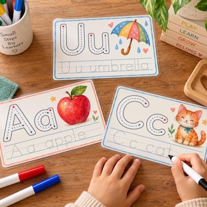 May include: Three rectangular educational alphabet tracing cards featuring the letters U, A, and C. Each card displays a large letter with directional arrows, a corresponding illustration of an umbrella, apple, or cat, and the word written in dotted lines.