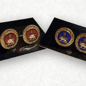 Puede incluir: Cuatro gemelos circulares con un borde dorado texturizado. Dos gemelos tienen un centro rojo con un emblema dorado de un león y un sol, mientras que los otros dos tienen un centro azul con el mismo diseño de león y sol en dorado.