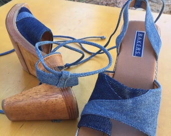 May include: A pair of blue denim platform sandals with wooden heels and lace-up closures. The sandals have a brown leather insole and are labeled "BAKKERS".