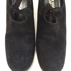 May include: A pair of black suede shoes with a lace-up design. The shoes have a round toe and a low heel. The brand name "Shoe Biz I.Magi" is printed on the inside of the right shoe.