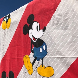 May include: A red and white striped fabric with a black and white cartoon image of Mickey Mouse. Mickey Mouse is wearing red shorts and yellow shoes.