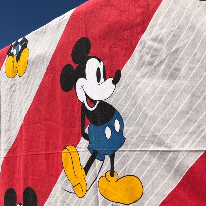 May include: A red and white striped fabric with a black and white cartoon image of Mickey Mouse. Mickey Mouse is wearing red shorts and yellow shoes.