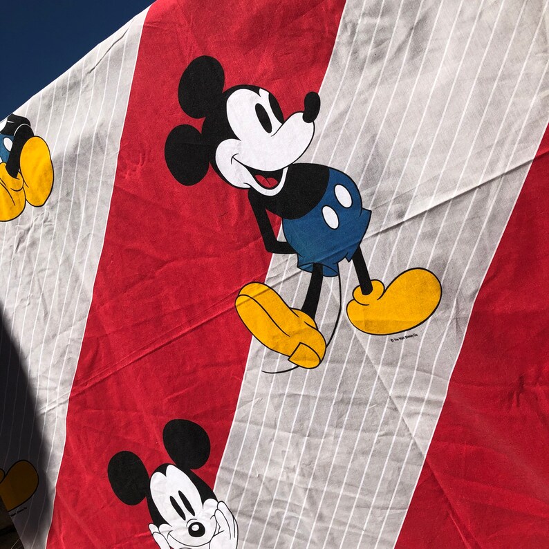 May include: Red and white striped fabric with two black and white Mickey Mouse characters. The Mickey Mouse characters are smiling and have black eyes and red cheeks. The fabric is a cotton blend.
