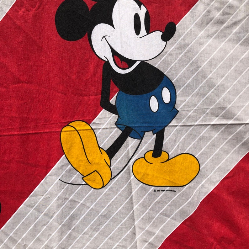 May include: A black and white cartoon image of Mickey Mouse wearing red shorts and yellow shoes. The background is red and white stripes.