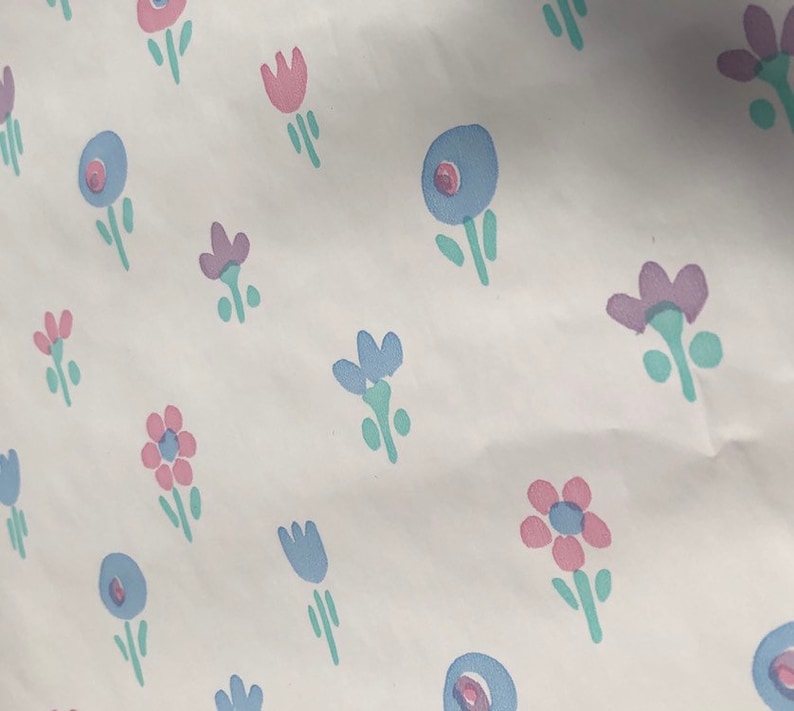 May include: White background with a repeating pattern of stylized flowers in pink, blue, and purple. The flowers have green stems and leaves. The design is simple and whimsical.