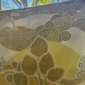 May include: A sheer curtain with a nature-inspired design. The curtain features a stylized tree with large, olive-green leaves and a yellow sun. Swirling cloud-like patterns in shades of brown and gray complete the design. The curtain is hanging in front of a window.
