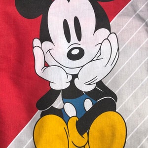 May include: A cartoon image of Mickey Mouse with black ears and a black outline. Mickey is sitting with his hands on his cheeks and a big smile. He is wearing yellow shoes and a blue shirt. The background is red and gray.