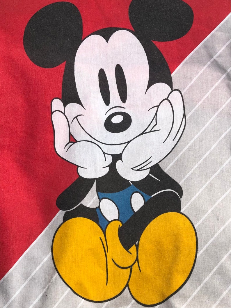 May include: A cartoon image of Mickey Mouse with black ears and a black outline. Mickey is sitting with his hands on his cheeks and a big smile. He is wearing yellow shoes and a blue shirt. The background is red and gray.