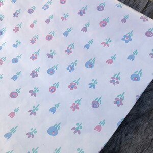 May include: White wrapping paper with a repeating pattern of small, stylized flowers in pink, blue, and green. The flowers are arranged in a scattered layout across the paper's surface.