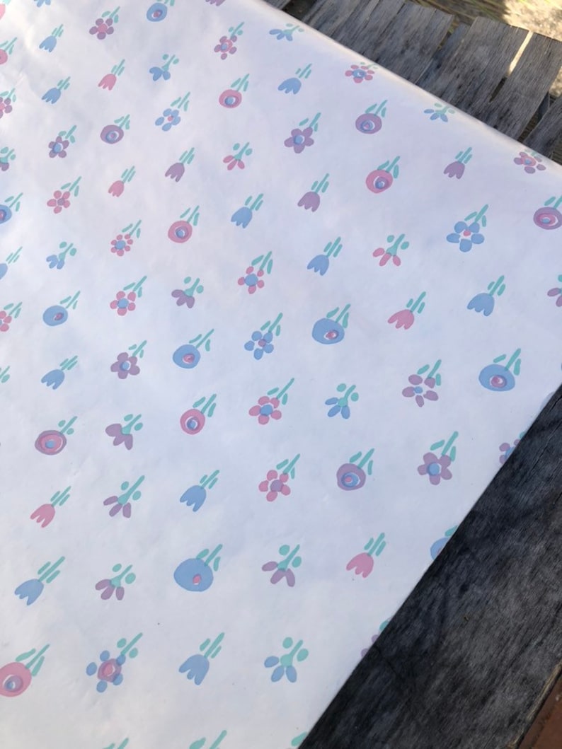 May include: White wrapping paper with a repeating pattern of small, stylized flowers in pink, blue, and green. The flowers are arranged in a scattered layout across the paper's surface.