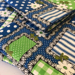 May include: A stack of blue and green fabric with a patchwork design. The fabric features white polka dots, white stripes, and white flowers.