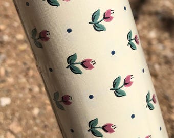 Puede incluir: Un objeto cilíndrico con una superficie de color crema que presenta un patrón repetitivo de pequeños tulipanes rosas con hojas verdes y diminutos puntos azul oscuro dispersos entre los motivos florales en todo el exterior.