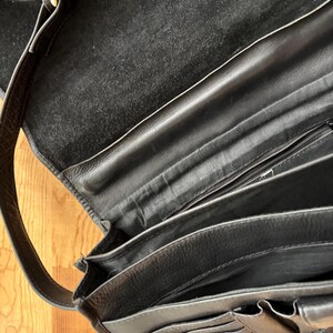 Puede incluir: Bolso de hombro de cuero negro con m&uacute;ltiples compartimentos y una correa larga. El bolso presenta una hebilla dorada y un cierre a presi&oacute;n. El interior est&aacute; forrado con un material suave y oscuro.