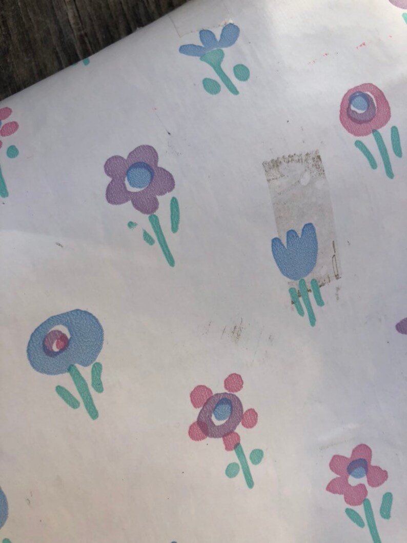 May include: White paper with a repeating pattern of stylized flowers in shades of purple, blue, and pink. The flowers have green stems and leaves. The paper has some discoloration and a piece of tape.