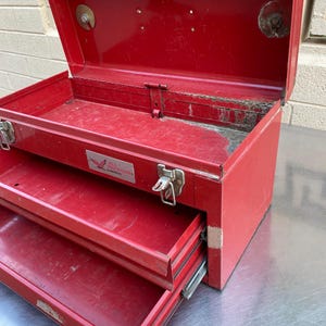 May include: Red metal toolbox with two drawers and a hinged lid. The toolbox has a label that reads "Bill Brown - Milwaukee, WI".