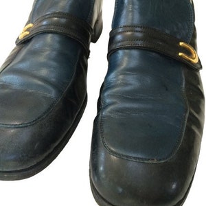 May include: A pair of dark blue leather slip-on shoes with black trim and gold buckles.