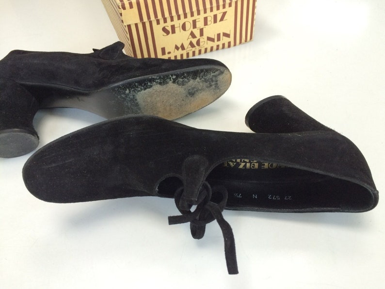 May include: A pair of black suede heeled shoes with a lace-up detail. The shoes are labelled "Shoe Biz at I. Magnin" on the inside.