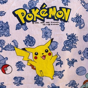May include: White fabric with a blue and yellow Pokemon print. The print features a yellow Pikachu character and the text "Pokemon" with the copyright information "© 1995, 1996, 1998 Nintendo. TM & © Nintendo."