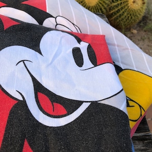 May include: Close-up of a red, white, and black Mickey Mouse character printed on a fabric. The fabric has a striped pattern in white and gray.