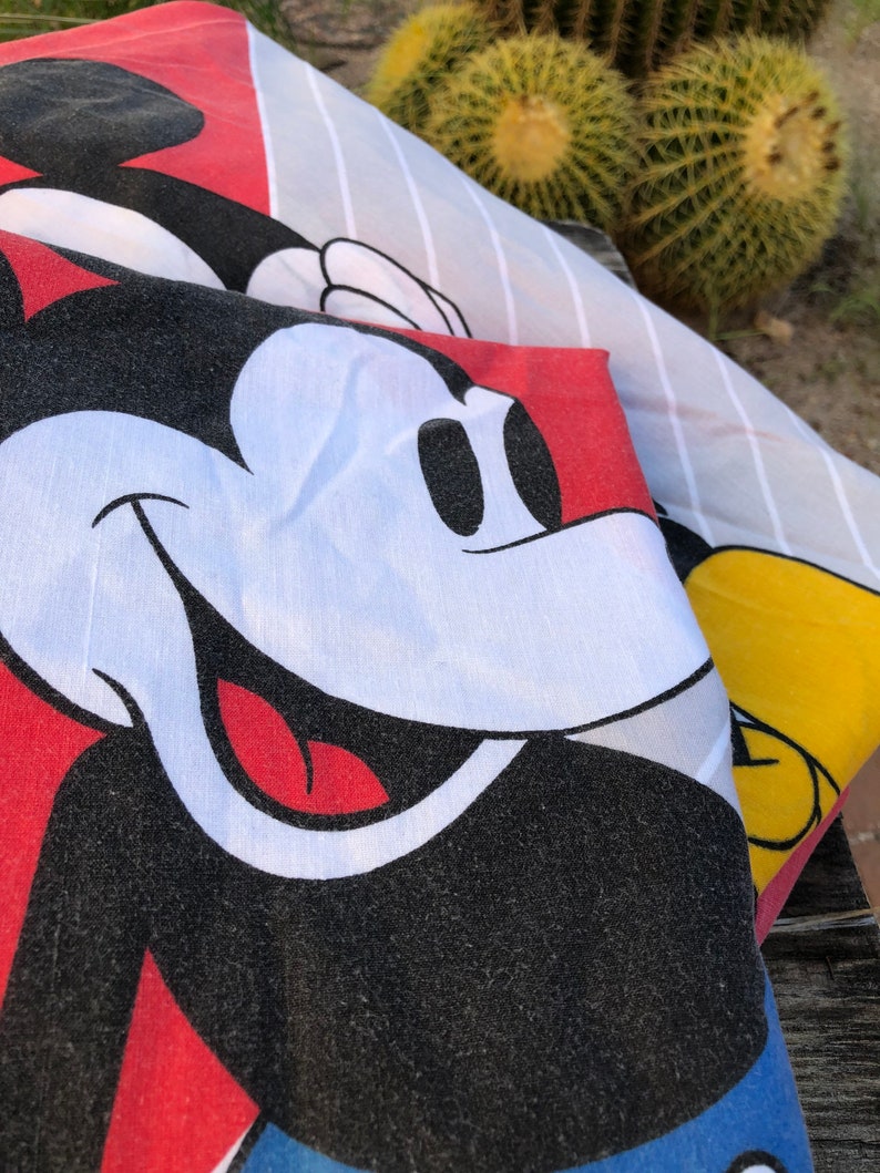 May include: Close-up of a red, white, and black Mickey Mouse character printed on a fabric. The fabric has a striped pattern in white and gray.