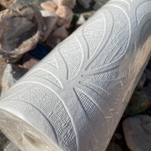 May include: A roll of white textured wallpaper with a repeating pattern of leaves. The wallpaper is rolled up and has a plastic covering.
