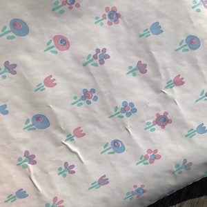 May include: White paper with a repeating pattern of small, stylized flowers in pastel colors. The flowers are in shades of pink, blue, and purple, with green stems and leaves. The paper has a slightly wrinkled texture.