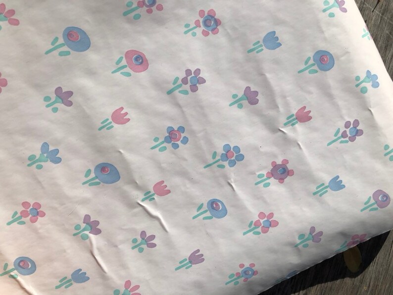 May include: White paper with a repeating pattern of small, stylized flowers in pastel colors. The flowers are in shades of pink, blue, and purple, with green stems and leaves. The paper has a slightly wrinkled texture.