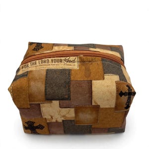 May include: A rectangular fabric pouch featuring a patchwork pattern in shades of brown and tan. The design includes silhouettes of deer, black crosses, and a rectangular label printed with the text: FOR THE LORD YOUR GOD WILL BE WITH YOU WHEREVER YOU GO - JOSHUA 1:9.