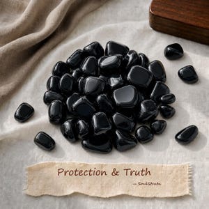 Puede incluir: Una colección de piedras de obsidiana negra pulidas con una superficie lisa y reflectante. Una etiqueta de papel rectangular en la parte inferior presenta el texto Protection & Truth y la marca SoulStrata en una fuente serif marrón oscuro.
