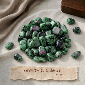 Pode incluir: Uma coleção de pedras de zoisite polidas com padrões salpicados de verde e preto e inclusões magenta vibrantes. Uma etiqueta de papel retangular abaixo das pedras apresenta o texto impresso "Growth & Balance" seguido de "- SoulStrata".